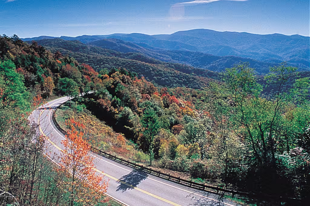 The Cherohala Skyway curving through autumn colour under a clear sky, mountains beyond